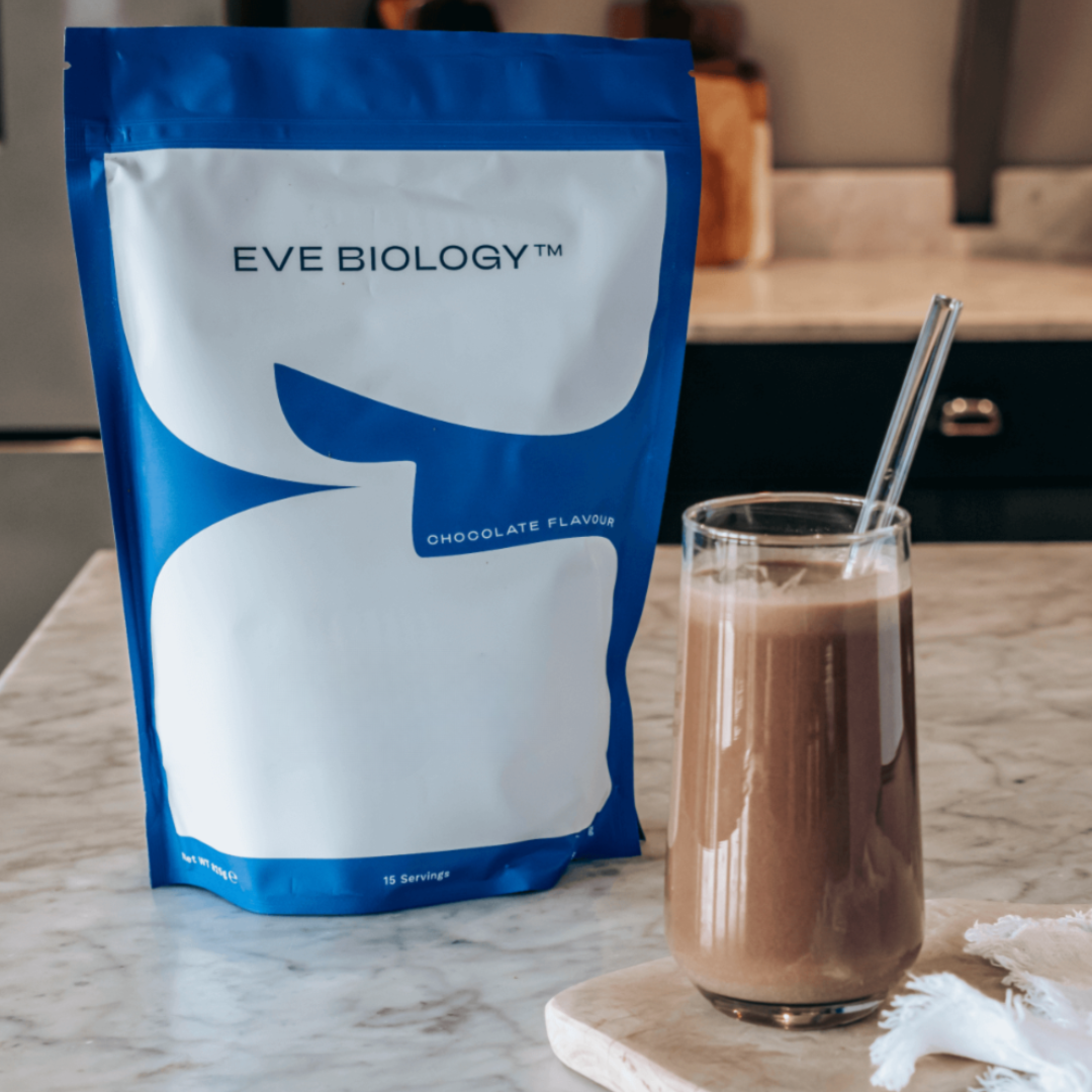 Eve Biology chocolate-flavored powder package next to a glass of chocolate milk on a marble surface.