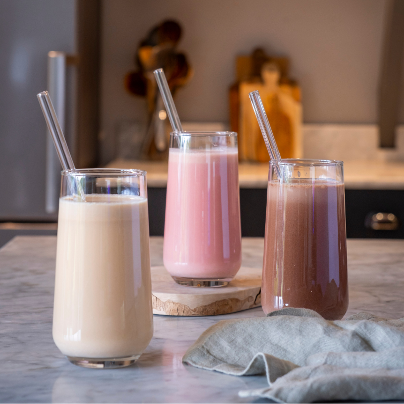 Three glasses of different flavoured shakes with straws on a marble surface.
