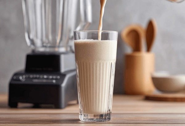 Blender pouring a creamy shake into a glass on a wooden surface.
