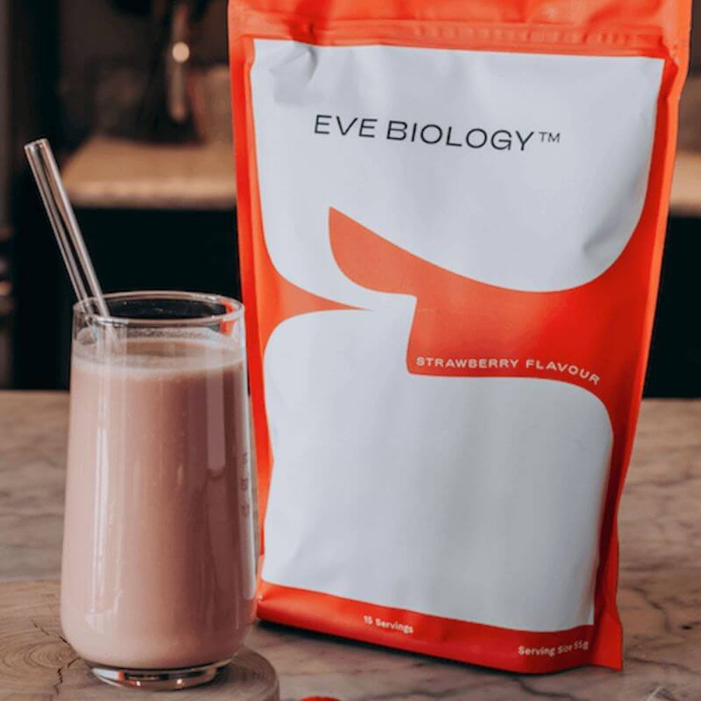 Eve Biology strawberry-flavoured shake package with a shake in a glass on a wooden surface.