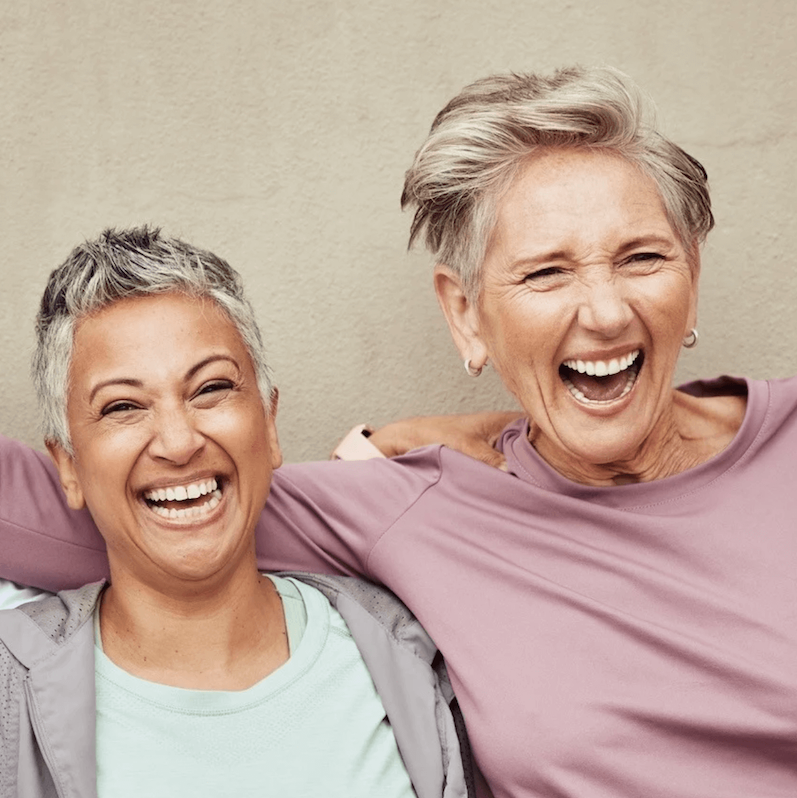 Two midlife women in casual clothing  laughing on a plain background