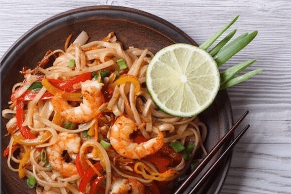 Noodles with shrimp and vegetables on a plate with a lime wedge and garnish.