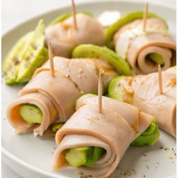 Rolls turkey and avocado with toothpicks on a white plate