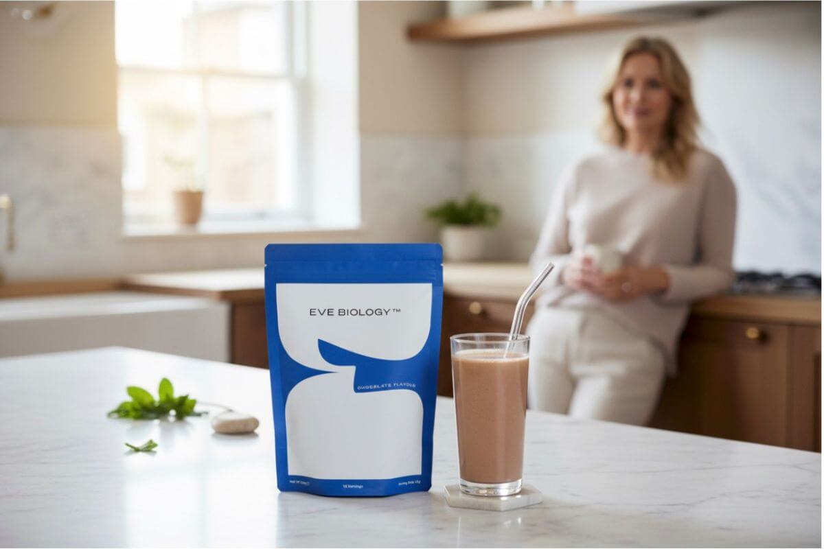 Woman in a kitchen with a chocolate shake and a pouch  labeled 'Eve Biology' on a counter.