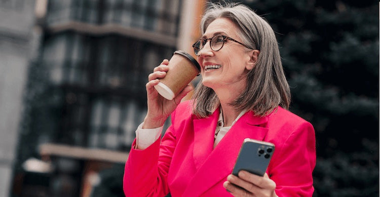 Woman in a pink blazer holding a coffee cup and phone outdoors.