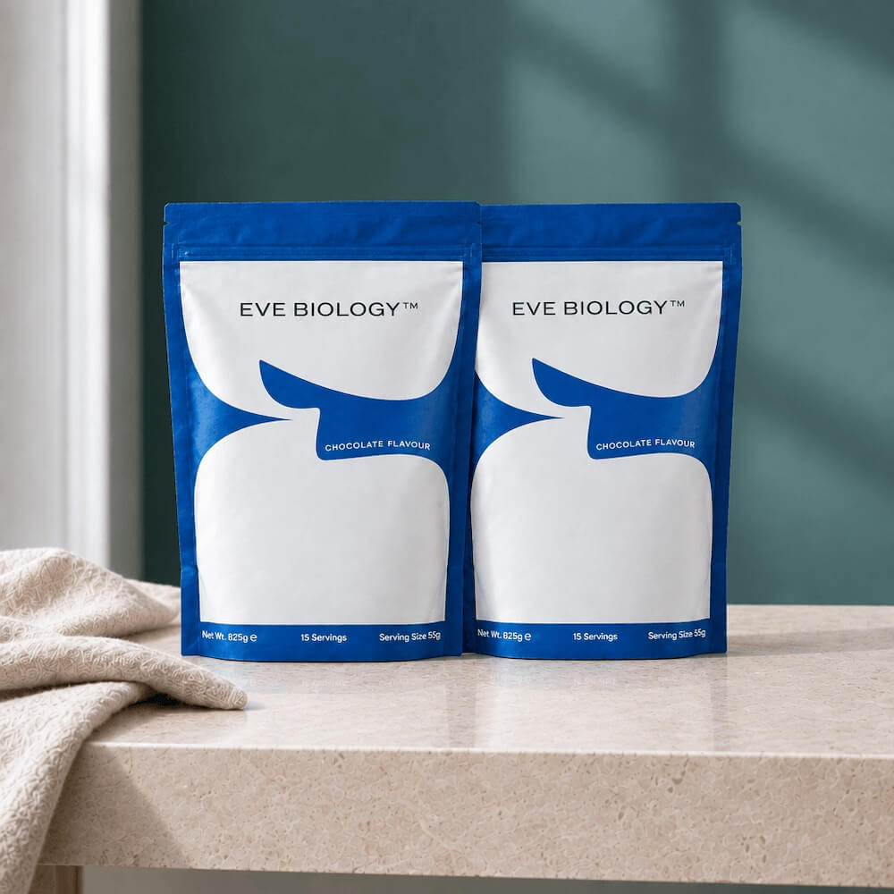 Two pouches of Eve Biology Meal Replacement Shakes on a counter top against a teal background