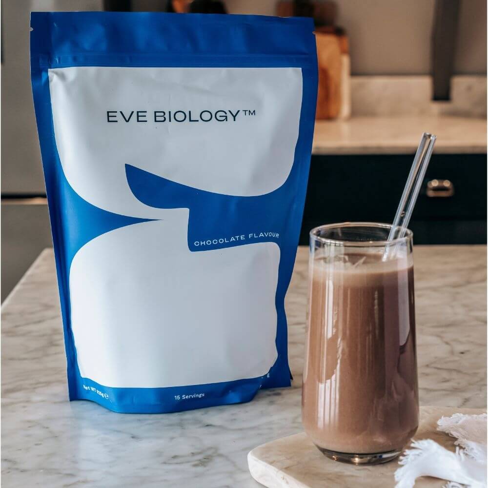 Eve Biology chocolate-flavored powder pouch next to a glass of chocolate shake on a marble countertop.