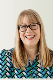 Person with glasses and a patterned shirt against a plain background