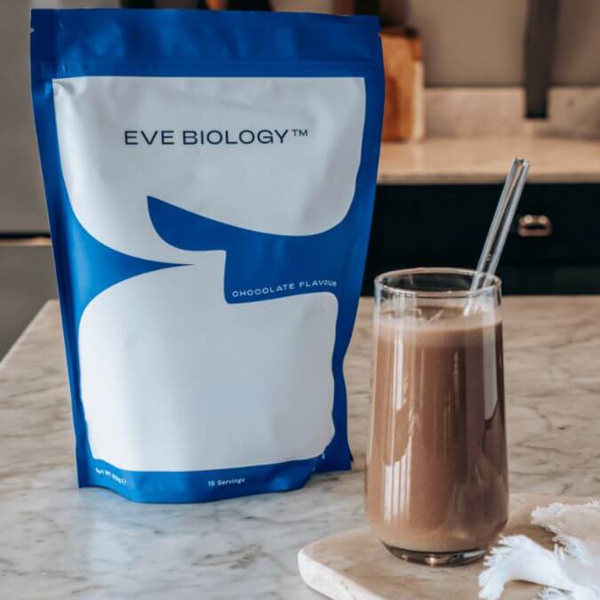 Eve Biology chocolate-flavored powder package next to a glass of chocolate shake on a marble surface.