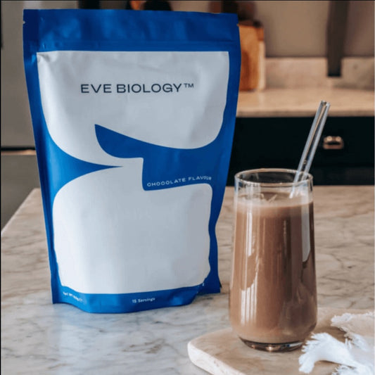 Eve Biology chocolate-flavoured shak pouch next to a glass of chocolate shake on a marble surface.