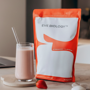 Eve Biology strawberry banana protein powder package with a glass of pink shake on a wooden surface.
