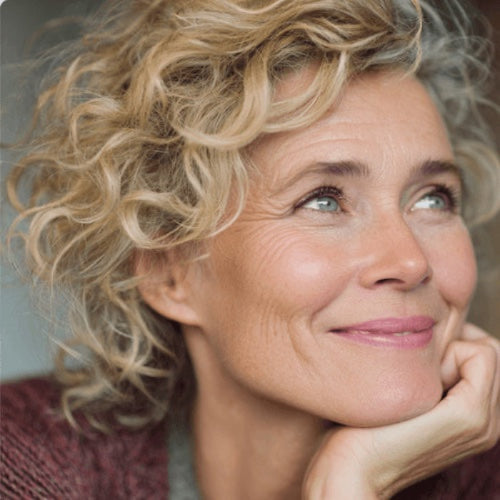 Woman with curly blond hair, gentle smile, hand holding face