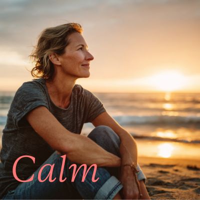 Woman sitting on a beach in a grey top watching sunset