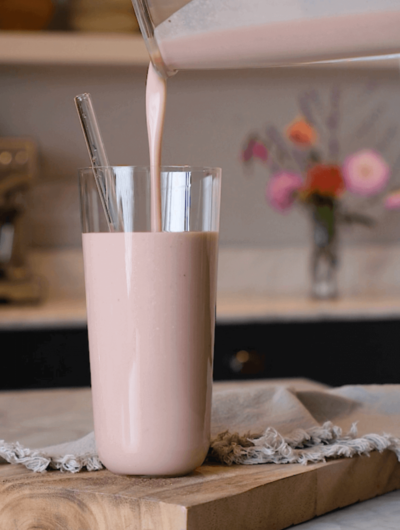 Pink meal replacement shake poured into a glass with a kitchen background