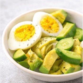 Salad with avocado and hard-boiled eggs in a white bowl on a light background