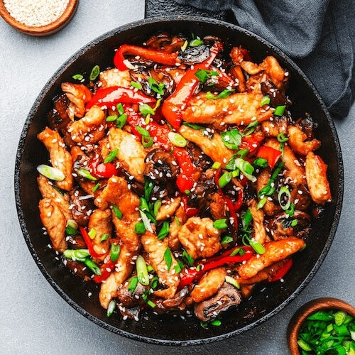 Fried chicken with vegetables in a black skillet on a light gray background