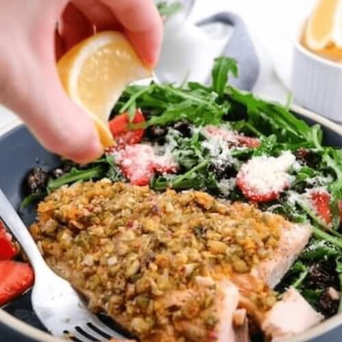 Salad with salmon and arugula being garnished with lemon.