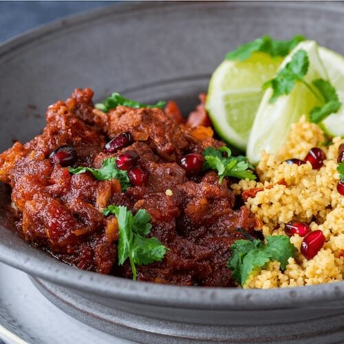 Dish with meat, couscous, and lime wedges on a gray plate