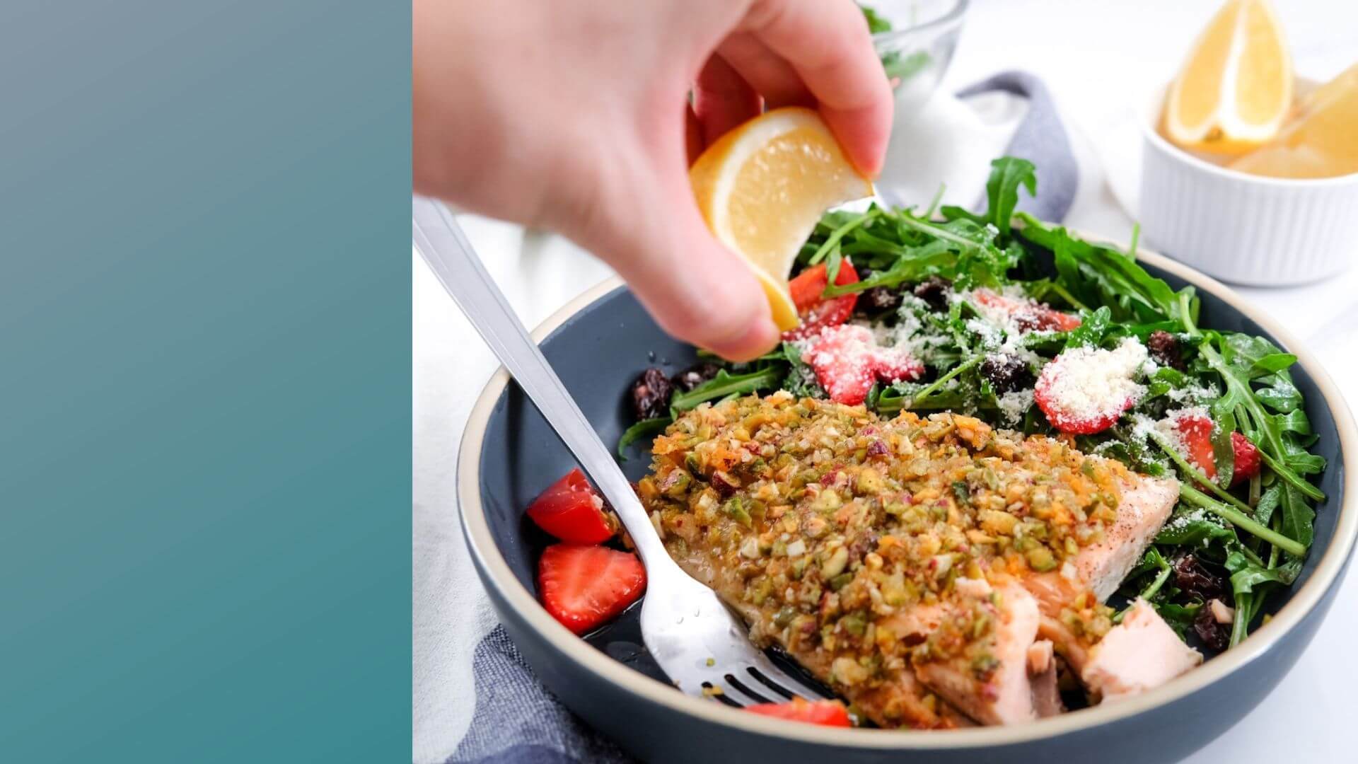 Hand squeezing lemon over a salad with salmon in a bowl.