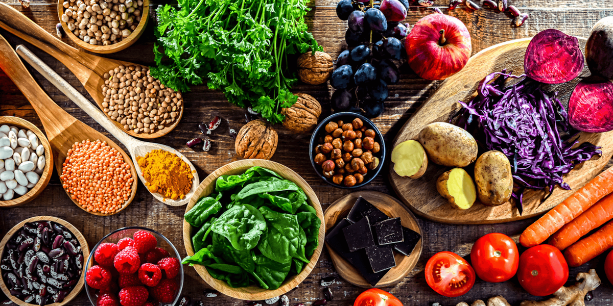 Assorted healthy foods including fruits, vegetables, and grains on a wooden surface.