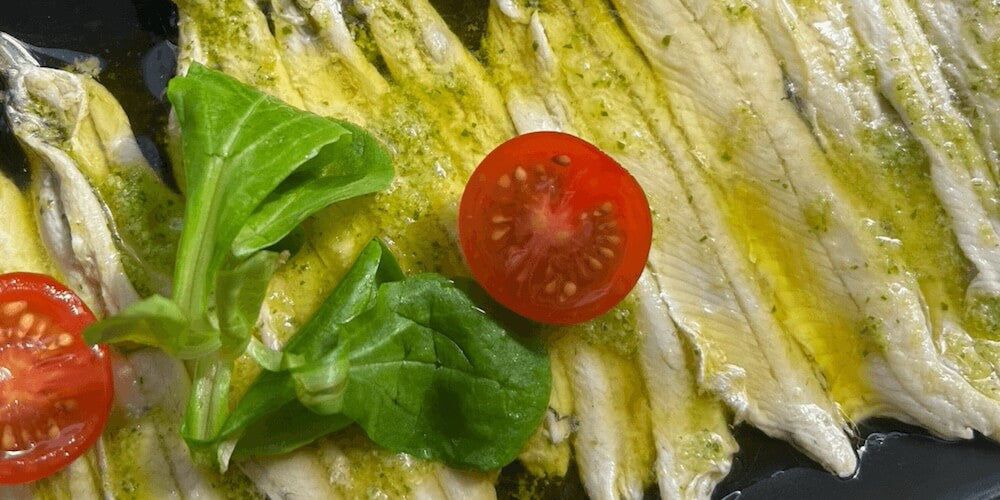 Anchovies with olive oil, tomato and basil on a black plate