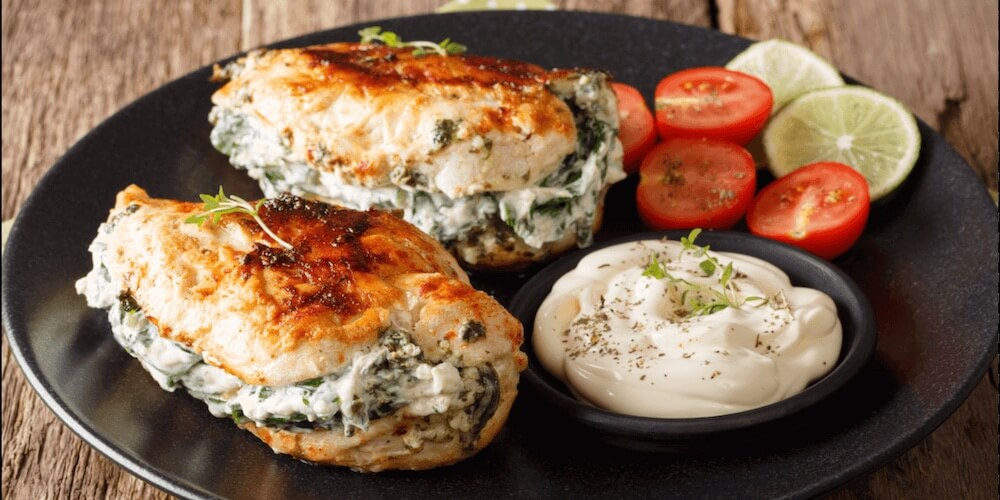 Cream cheese and herb stuffed chicken breasts on a black plate
