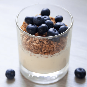 Glass container with yogurt, granola, and blueberries on a light background