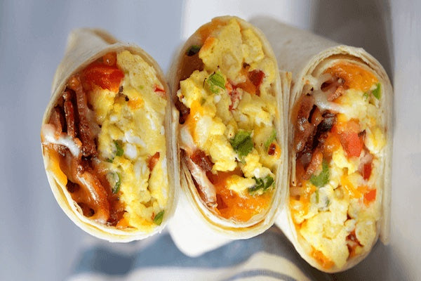 Three burritos filled with scrambled eggs and ham on a white surface