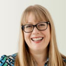 Woman with glasses and a smile against a plain background