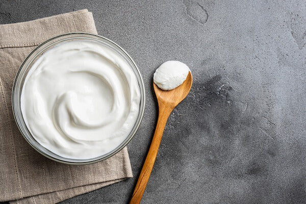 Glass bowl of yogurt with a wooden spoon on a gray surface