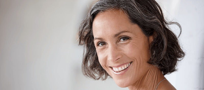 Woman with short brown hair smiling against a light background