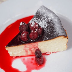 Slice of cheesecake with berries and red sauce on a white plate