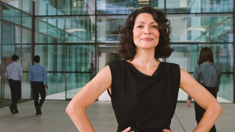 professional woman, smile on face, hands on hips, in office building