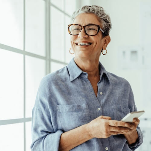 Woman wearing glasses and a blue shirt, holding a phone indoors.