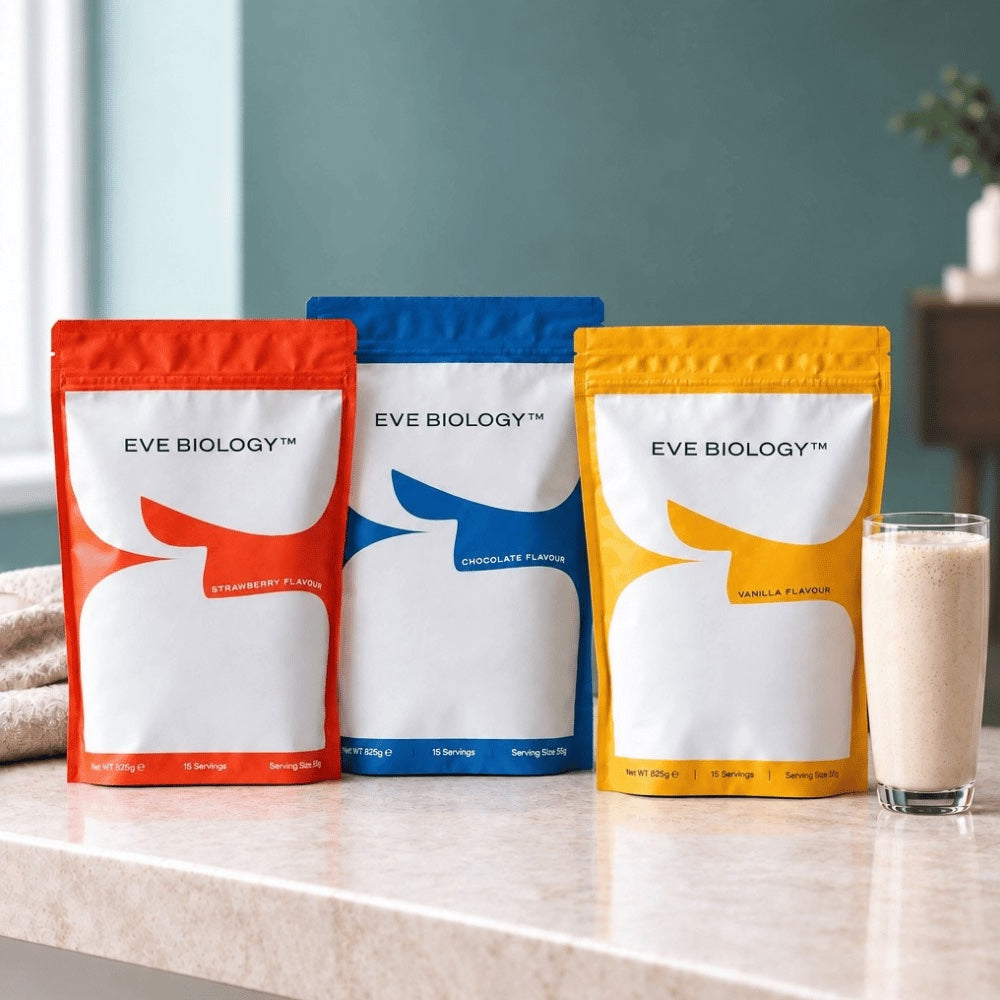 Three stand-up pouches of Eve Biology protein powder in red, blue, and yellow packaging, displayed on a light marble countertop with a glass of milkshake beside them.