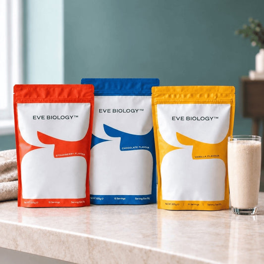 Three stand-up pouches of Eve Biology protein powder in red, blue, and yellow packaging, displayed on a light marble countertop with a glass of milkshake beside them.