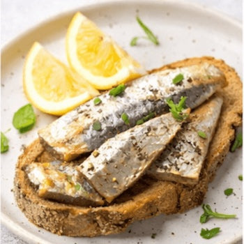 Slices of sardines on toast with lemon wedges on a white plate