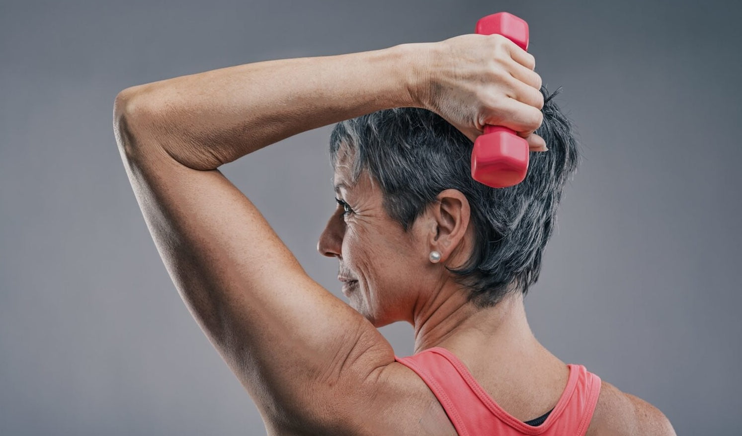 Woman exercising with a pink dumbbell against a gray background