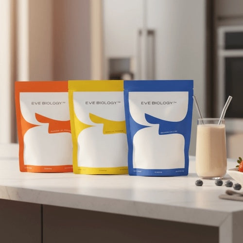 Three Eve Biology packages in orange, yellow, and blue on a kitchen counter with a glass of shake.