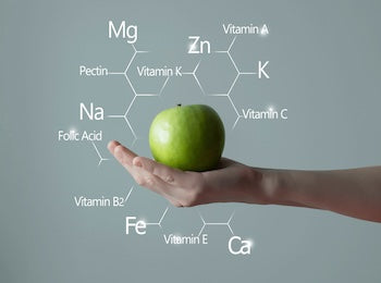 Hand holding a green apple with nutritional element labels on a gray background