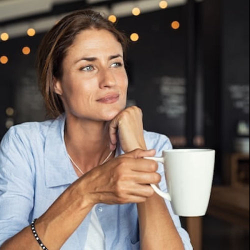 Woman holding a white mug in a cozy indoor setting with string lights.